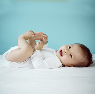 Bebé de 1 a 3 meses en la cama boca arriba jugando con los pies.